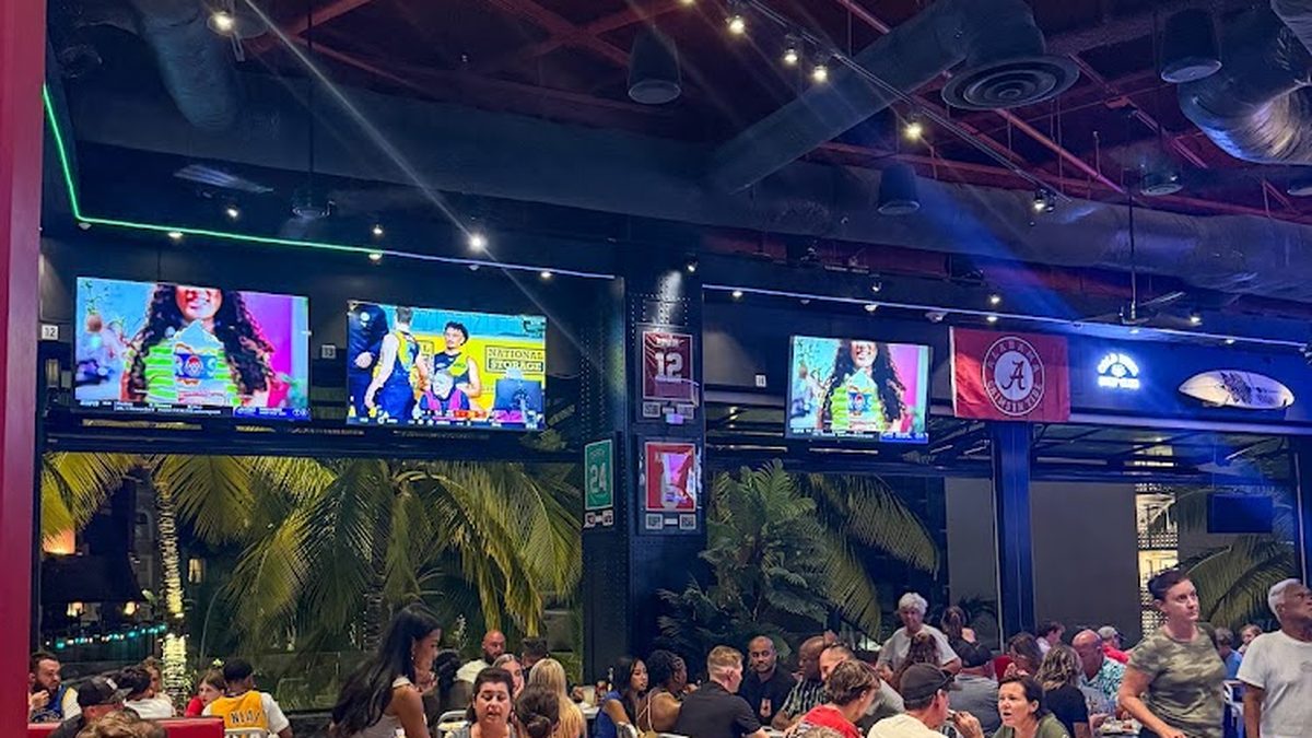Packed crowd at Skybox Taphouse Waikiki with palm trees and TVs at night